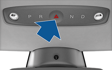 Селектор режимов движения на потолочной консоли со стрелкой, указывающей на кнопку аварийной сигнализации в центре.